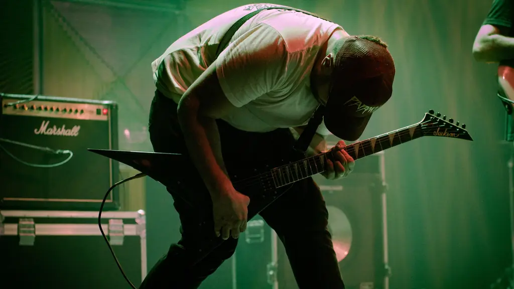 Guitarist bent over his instrument under green stage light