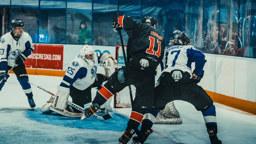 Hockey players crashing the net in front of a sprawling goalie