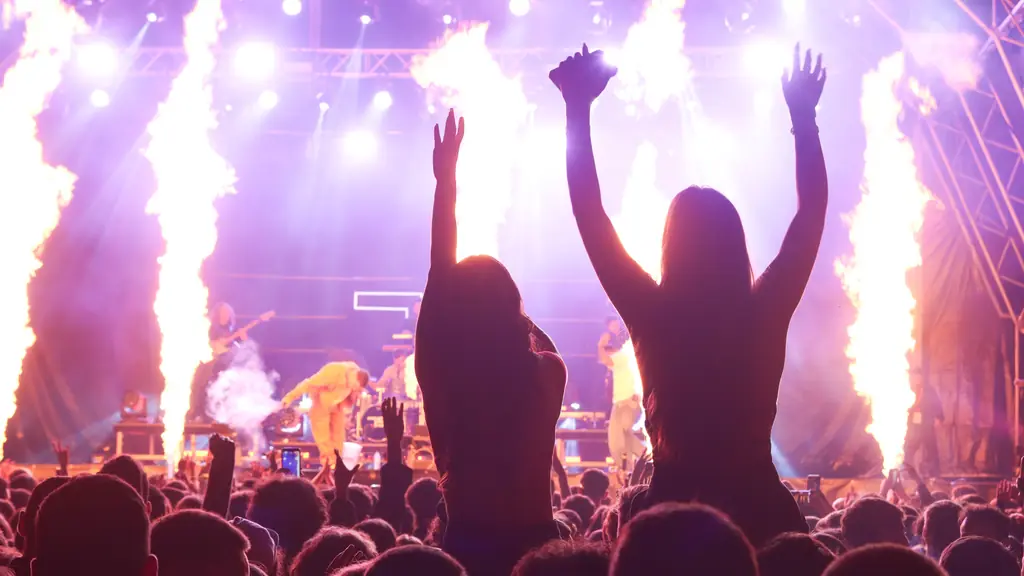Crowd with raised arms in front of a stage shooting columns of fire