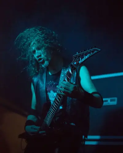 Long-haired guitarist lit in blue, mid-solo